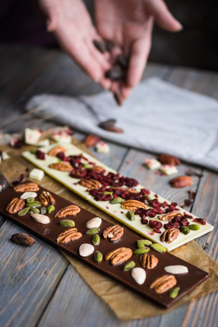 why-choose-us Gourmet chocolate bars topped with almonds, pecans, and cranberries on wooden background.